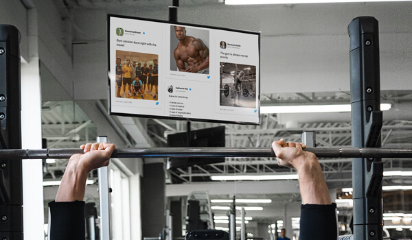 A digital screen shows a collage of social media posts shared by gym members using a social wall solution
