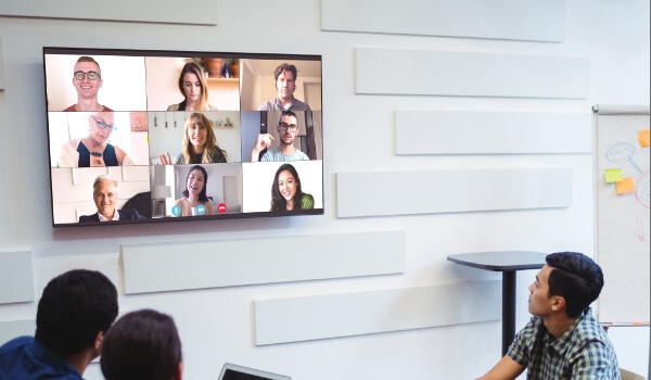 A team communicates virtually with remote employees on a large conference room digital signage