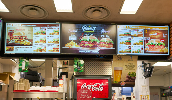A series of digital menu boards inside a quick serve restaurant shows a variety of burgers and deals on selected items