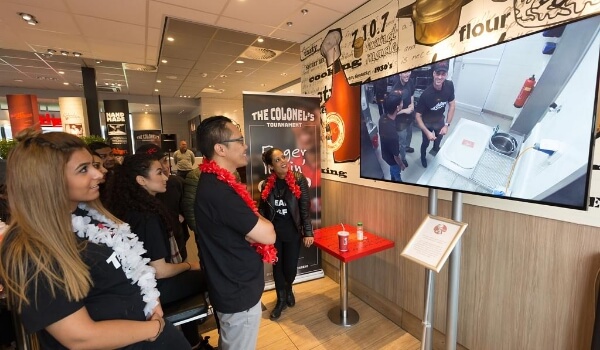 An office event is streaming live on digital signage screen and employees are watching it