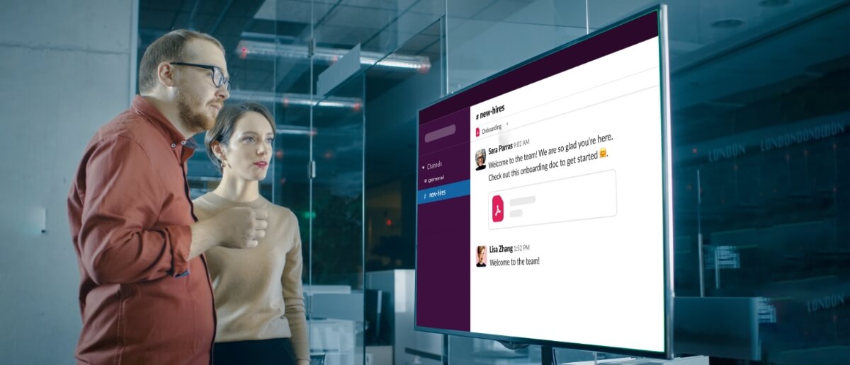 Employees in an office reading messages on Slack dashboard displayed on digital signage screen