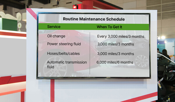 An automobile dealership showroom displays a car maintenance schedule on a large digital signage screen