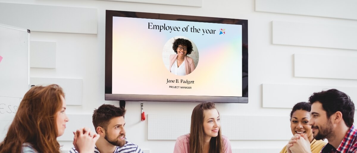 office employees having a discussion in a meeting room with a digital signage screen which displays employee of the month