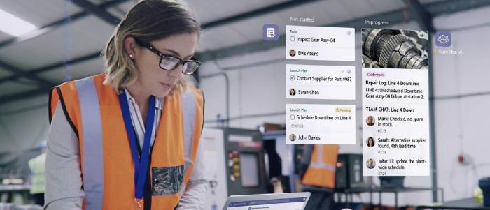 Frontline workers in a manufacturing facility viewing a digital communication screen displaying shift briefings and company updates