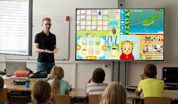 Students in a classroom are engaging with the game-based lessons shown on digital signage screen