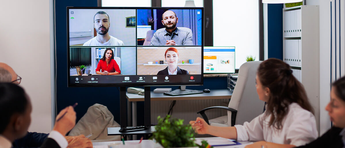 group of employees having a discussion in a meeting room with digital signage screen displaying online video conferencing app with members