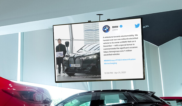 An automobile dealer digital signage displays the Twitter post of BMW. The tweet shows a photo of a customer winning a black BMW