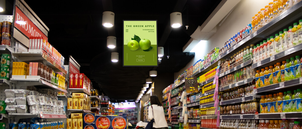 A convenience store digital signage near the product shelves promotes offers on fresh apples
