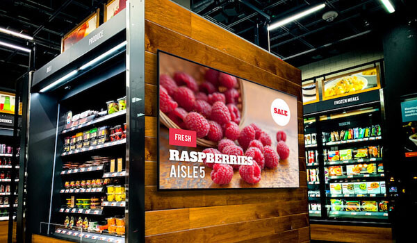 A large LED screen inside a grocery supermarket store promotes a sale on fresh raspberries