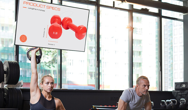 People work out at a fitness center. A large screen in the background shows the specifications of a set of red dumbbells