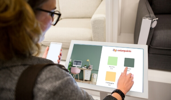 A woman browses paint color from a digital product catalog on an interactive kiosk