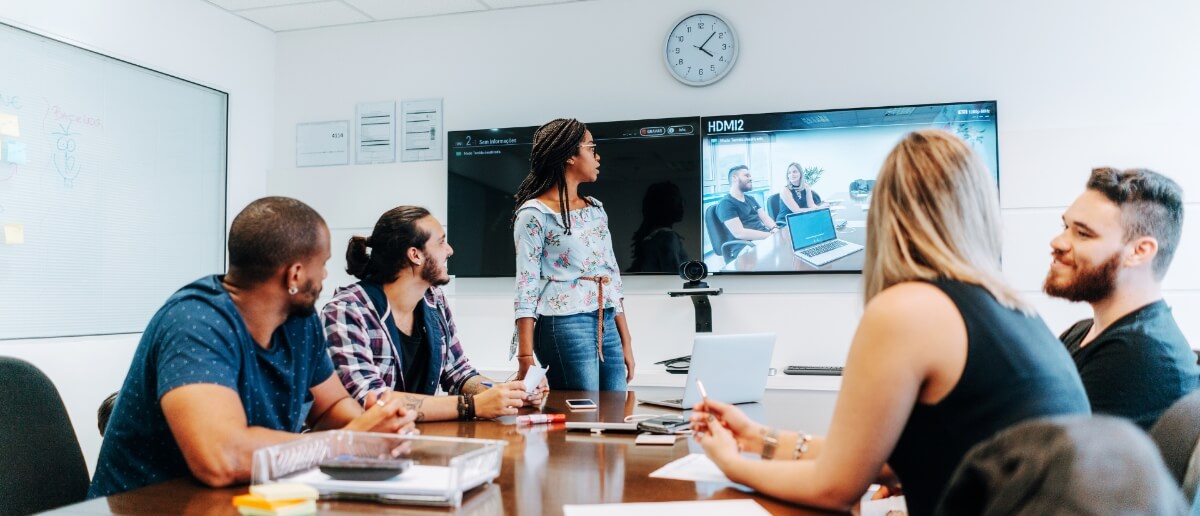 A team looks at a digital signage screen that shows them communicating virtually