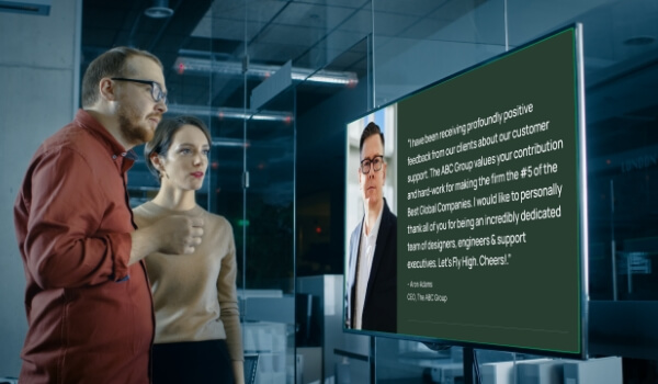 Two employees in an office read a letter from the CEO that is displayed on a large digital signage screen