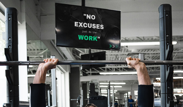 A gym digital signage shows motivational content as a member practices heavy weight lifting