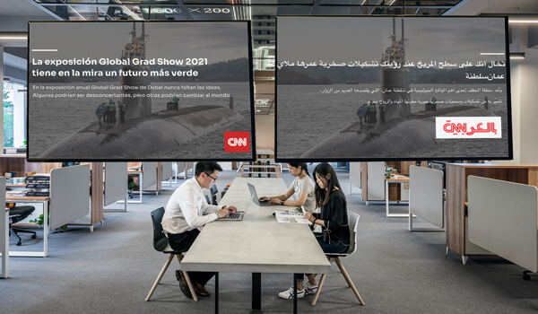 Two large digital displays installed in an office space show the same CNN news in Spanish & Arabic languages. An example of inclusive work culture
