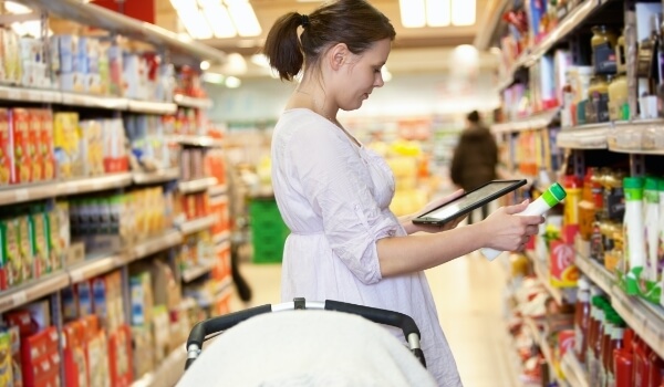 A woman holds a shampoo bottle & checks the product information of the same on her tablet