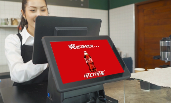 A woman at a restaurant works with a point of sale billing system while the customer facing iPad shows a coca-cola ad in Chinese