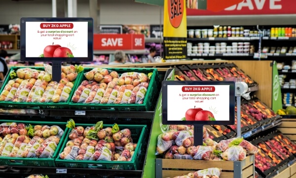 Two digital shelf display tablets near the point of sale of a grocery store promote attractive offers on apples