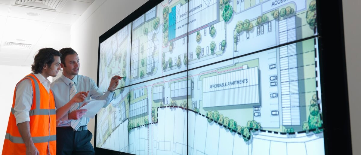 An architect & real estate engineer refer to an aerial shot of a plot shown on a large digital signage