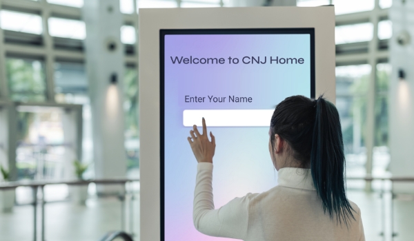 A woman logs her visitation details on a digital screen for self check-in into a building