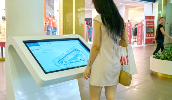 A consumer looking at a digital wayfinding kiosk inside a shopping mall