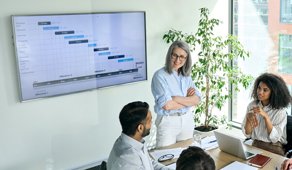 Employees are engaged in a discussion inside a corporate conference room that shows the weekly schedule on a sleek digital signage screen