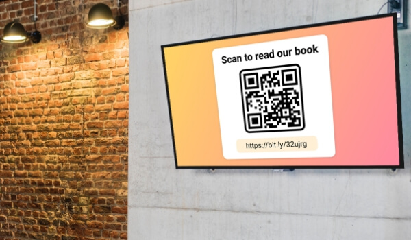 A digital signage TV inside an office break room shows a QR code and the text 'Scan to read our book'