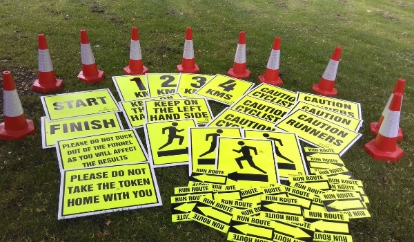 Many correx-made small portable sign boards lying on a field show black-&-yellow icons, numbers & words
