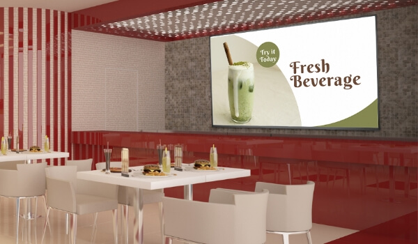 A restaurant promotes its fresh beverages on a large digital signage display near the dining tables