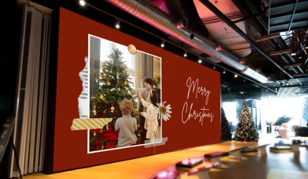 A large digital video wall inside an auditorium shows bright red Christmas message with images