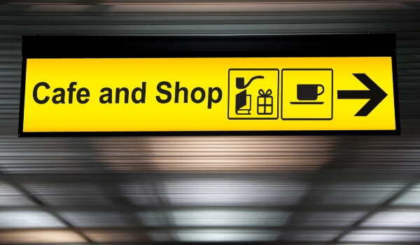 An illuminated ceiling-mount direction signage shows the way to the cafe & shops