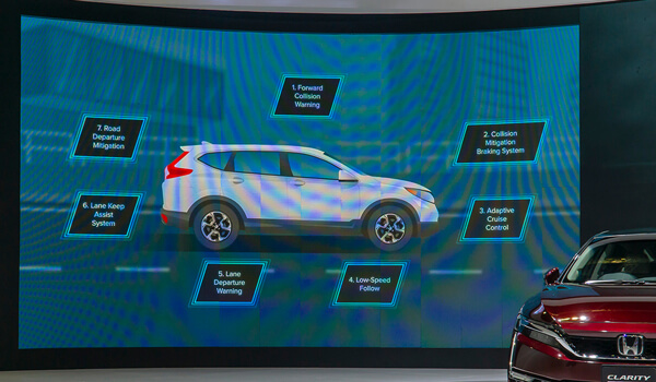 A video wall inside an automobile dealership shows specifications of an SUV model as a red Honda Clarity remains on display