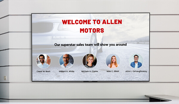 A wall-mounted digital display behind a car dealership reception welcomes its clients and introduces their sales team