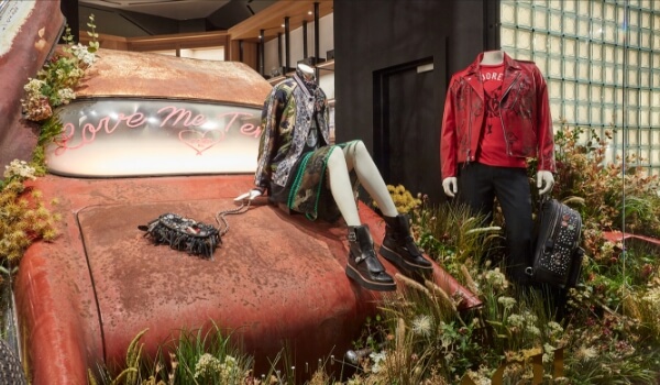 Coach's window display shows an Elvis-themed collection. The mannequins wear punk jackets & sit on a discarded car in the wilderness