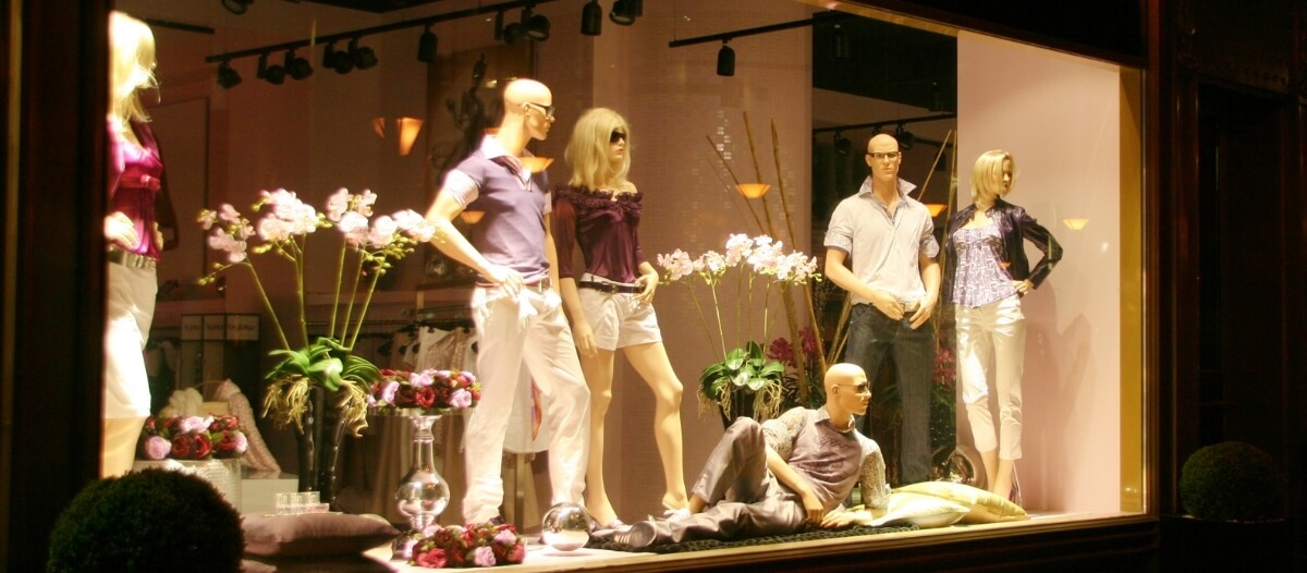 A fashion store window display shows mannequins arranged beautifully as part of the visual merchandising composition