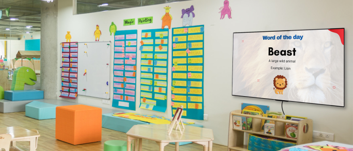 An elementary classroom digital signage shows ‘Word of the Day’. The Meaning of ‘Beast’ is shown with the image of a lion.