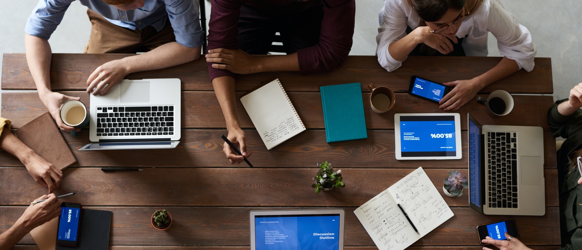 employees having a communication over a table with laptops, notebooks, and coffee